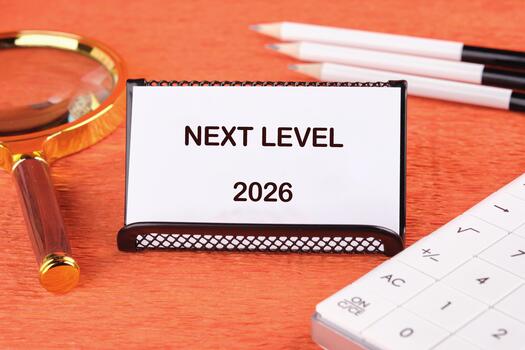 A desk scene captures a card labeled next level, resting on a vibrant orange surface. A magnifying glass, pens, and a keyboard suggest a focus on future goals and imaginative projects photo