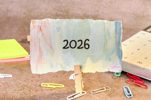 un vistoso tarjeta mostrando el año 2026 es retenida arriba por un pinza de ropa en contra un suave, texturizado fondo. papelería artículos rodear el escena, agregando un creativo toque foto