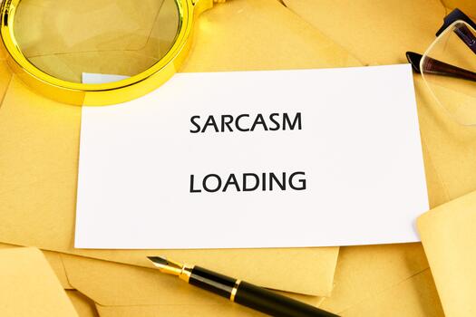 A humorous message on a card stating sarcasm loading is placed on a cluttered desk filled with envelopes, a magnifying glass, and a stylish pen, reflecting a playful office atmosphere photo