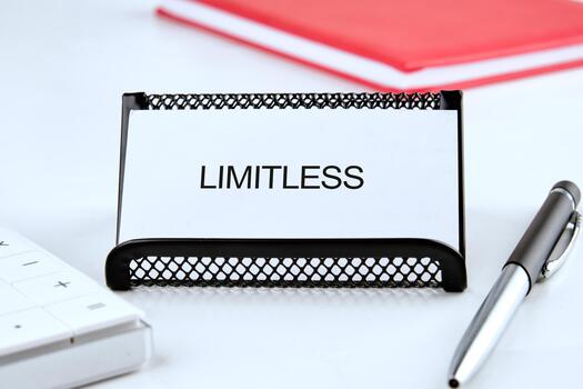A card displaying the word LIMITLESS lies on a neat desk surrounded by a pen and a keyboard. Bright red notes in the background suggest organization and focus on goals photo