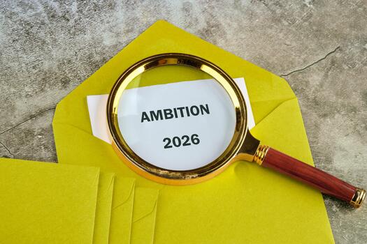 A yellow envelope holds a message about ambition for 2026, with a magnifying glass emphasizing the importance of future aspirations and planning for success photo