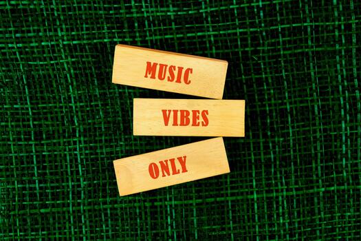 Three wooden blocks featuring bold red text express the lively message of music vibes only, set on a textured green backdrop that enhances their attention-grabbing appearance photo