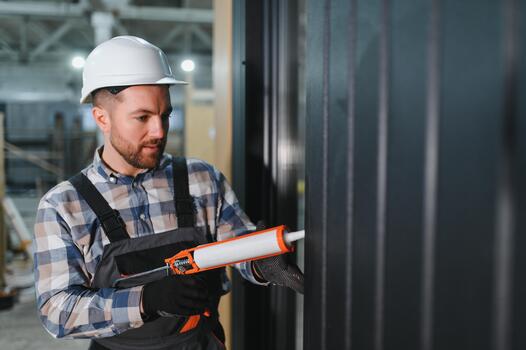 A worker is applying polyurethane foam to fill gap,between sash and window frame in prefabricated modular house photo