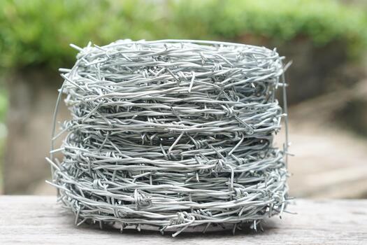 A close-up of a roll of shiny barbed wire placed on wooden surface with blurred green background. Symbol of security, protection, and boundary in agriculture or construction use. photo