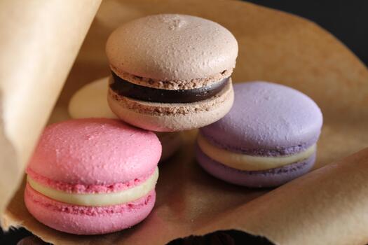 Tres 3 multicolor macarrones mentira en hecho a mano marrón papel siguiente a mentira almendra palos canela y café en un negro antecedentes con sitio para texto y con un copyspace foto