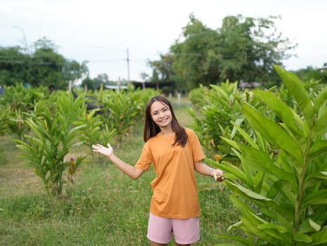 Young woman smiling in a green field with plants, wearing a casual outfit and enjoying a sunny day outdoors, surrounded by nature and growth photo