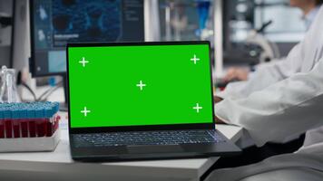 mayor científico utilizando verde pantalla ordenador portátil software en laboratorio, conducción tratamiento descubrimiento. asiático utilizando bioinformática solicitud en Bosquejo cuaderno en estéril laboratorio, cámara si video