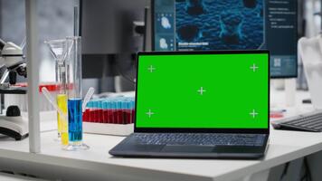 aislado pantalla ordenador portátil en laboratorio siguiente a prueba tubos y microscopio equipo. Bosquejo cuaderno en laboratorio usado a estudiar adn hebra cartografía con genómica análisis programa, enfocar fuera Disparo video