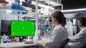 científico mecanografía en teclado, utilizando verde pantalla computadora programa en laboratorio, conducción tratamiento descubrimiento. experto utilizando bioinformática software en croma llave ordenador personal en estéril laboratorio, cámara un video