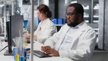 Scientist in laboratory interprets clinical blood values on computer monitor during study. Research facility worker doing sanguine fluid analysis, looking at healthcare insights report on PC, camera B video