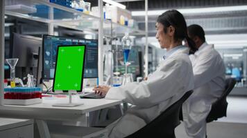 laboratorio experto a escritorio utilizando verde pantalla tableta, mirando a molecular modelo, haciendo investigación tareas. asiático hombre utilizando bioingeniería programa en Bosquejo dispositivo en médico laboratorio, cámara un video