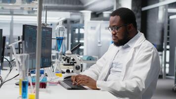 labb specialist håller på med genetik studie använder sig av klinisk Utrustning, avlägsnande glasögon, kontroll analys resultat på dator. man använder sig av vetenskaplig redskap på arbetsbänk, håller på med komplex experiment, kamera b video