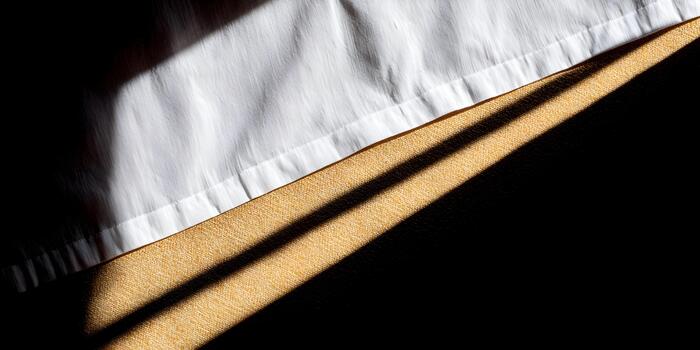 Sunlight casts strong diagonal shadows on white and yellow textured fabrics creating an abstract composition photo