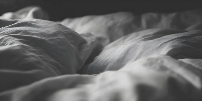 Close up view of rumpled bed sheets creating soft textures and shadows in a monochrome bedroom setting photo