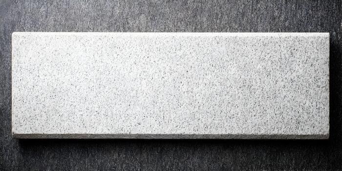 A rectangular light gray speckled granite block rests on a darker textured background photo
