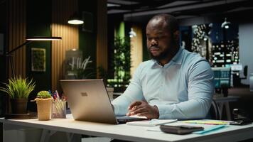 afrikansk amerikan kille skriver information på bärbar dator och kontroll rapporter, korrekturläsning och granskning data för en ny företag mål eller mål. företag förvaltning efter timmar. kamera a. video