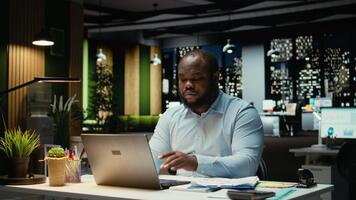 afrikansk amerikan kille granskning marknadsföra data och byggnad strategi för företag mål, använder sig av kalkylblad på bärbar dator för korrekturläsning. över tid efter timmar på multinationell företag. kamera a. video