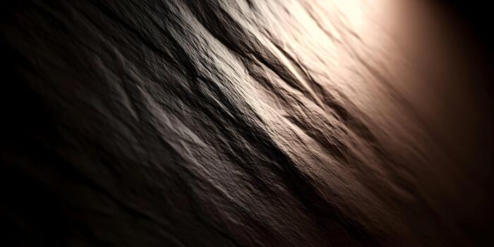A dark rough textured surface is dramatically illuminated by a warm diagonal light creating deep shadows photo