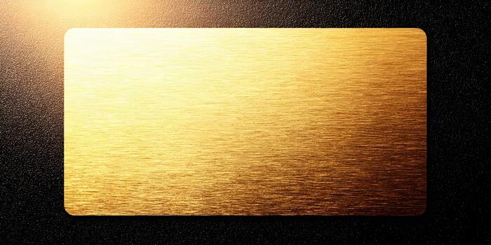 A shimmering golden brushed metal blank card or plaque is illuminated against a dark textured background photo