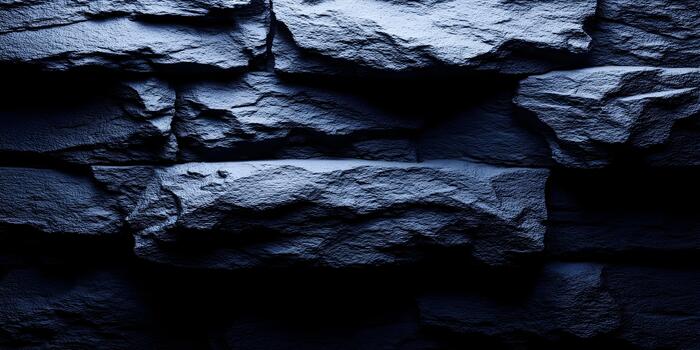 A dark blue rough stone wall texture features jagged rocks with dramatic light and shadow creating a moody abstract background photo