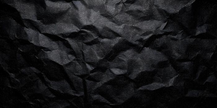 A dark abstract background features a heavily crumpled sheet of black paper creating a rough textured surface photo