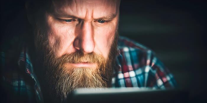 An intense bearded man with a furrowed brow concentrates on a task in a dark setting photo
