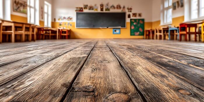 An empty elementary school classroom features a textured rustic wooden floor with blurred colorful furniture and a blackboard in the background photo