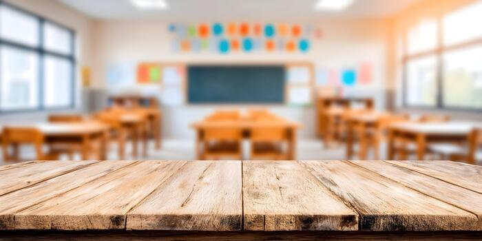 A rustic wooden table foreground sits before a bright blurred empty classroom background with desks blackboard and sunny windows photo