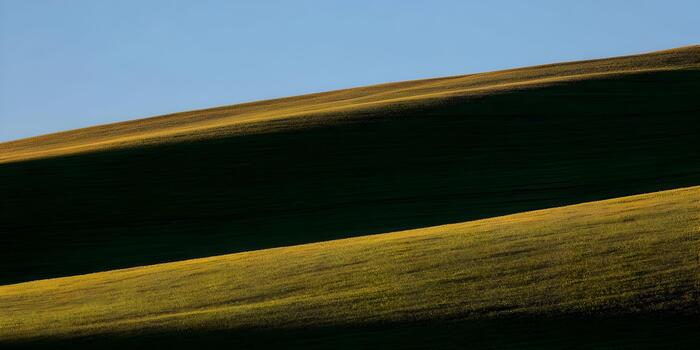 Sunlight illuminates the rolling green hills creating a beautiful abstract pattern of light and shadow under a clear blue sky photo