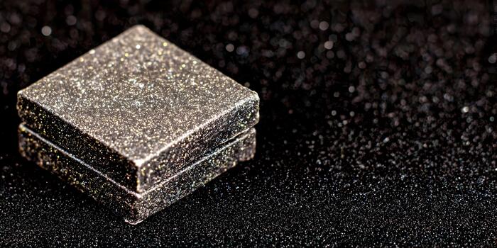 A close up of two dark rectangular objects covered in iridescent glitter and sparkles on a matching textured black background photo