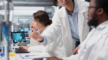 diagnóstico laboratorio gerente supervisando científicos mirando a molecular modelos en ordenador personal. equipo líder supervisando investigadores utilizando bioingeniería programa en computadora en médico laboratorio, cámara si video
