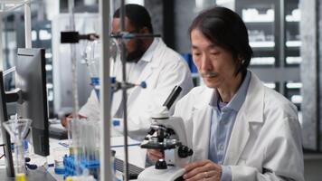 mikroskopist användningar förening mikroskop till studie genetisk material i kontrollerade laboratorium miljö. asiatisk biolog studier vävnad under optisk enhet till upptäcka, detektera sjukdom på tidigt skede, kamera b video