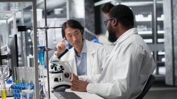 diagnostico laboratorio colleghi utilizzando microscopio per valutare cellulare strutture nel laboratorio. clinico microbiologi osservare medico fazzoletto di carta attraverso ingrandimento attrezzo a laboratorio panchina video