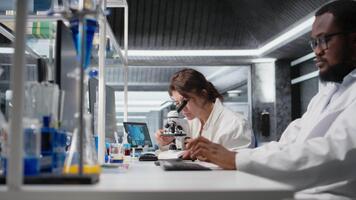 cytoteknolog justerar mikroskop, zoomar på cellulär strukturer i labb, studier genetisk störningar. molekyl biolog konstaterar mikroorganismer med förstoring verktyg på laboratorium bänk, kamera en video