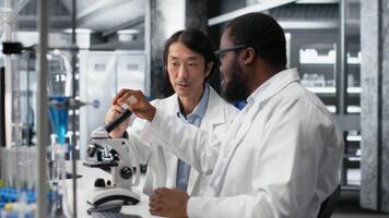 Clinical microbiologists using microscope to evaluate cellular structures in lab. Diagnostic laboratory colleagues observe medical tissue through magnification tool at workbench video