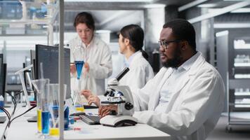 ricercatore operativo microscopio, fare campione osservazioni nel laboratorio, scrittura Appunti. scienziato studi fazzoletto di carta sotto ottico dispositivo nel biotecnologia laboratorio, segnalazione risultati, telecamera B video