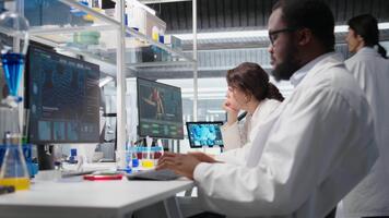 Laboratory manager oversees scientists working on computer, processing DNA data. Lab team leader and employees looking at genetic analysis diagnostics, brainstorming scientific breakthroughs, camera A video