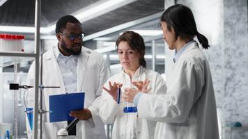 multirazziale chimici utilizzando ricerca servizio, struttura fiale pieno con indicatore soluzione. lavoro di gruppo laboratorio professionisti utilizzando chimico fluido test tubi per esperimenti, telecamera B video