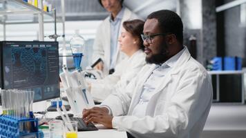 retrato de contento científico mecanografía en teclado, utilizando computadora programa para adn datos análisis en laboratorio conducción tratamiento descubrimiento. alegre investigador utilizando bioinformática software en laboratorio, cámara si video