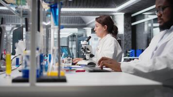 utmattad laboratorium molekyl biolog stretching på pc skrivbord, bearbetning dna patient data. trött labb anställd stängning ögon, tar ha sönder från genetisk analys på dator till koppla av, kamera en video