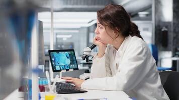 aburrido médico laboratorio técnico utilizando computadora solicitud para adn datos análisis. perezoso investigación instalaciones trabajador utilizando bioinformática genómica programa en ordenador personal en alto tecnología laboratorio, cámara si video
