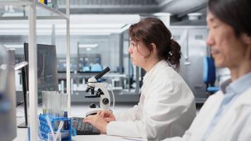 Nanotechnology researcher checking time, waiting to finish shift, processing patient data. Lab employee using PC to do genetic analysis diagnostics checking wrist watch clock, camera B video
