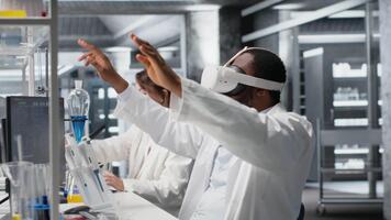 forskare använder sig av dator och vr headsetet Utrustning för dna data analys i laboratorium. afrikansk amerikan man använder sig av bioinformatik genomik programvara och virtuell verklighet tech i modern labb, kamera b video