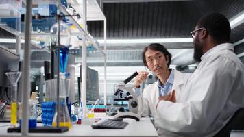 team av multietnisk mikrobiologer arbetssätt tillsammans i labb med molekyl mikroskop. raser kollegor i forskning anläggning använder sig av optisk enhet redskap till undersöka medicinsk vävnad, kamera en video