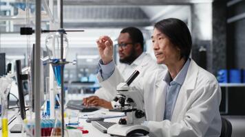 senior labb ingenjör inspekterande prov glida för mikroskopi studie använder sig av optisk enhet. medicinsk laboratorium tekniker granskning cytologi glida för klinisk testning procedur, kamera b video