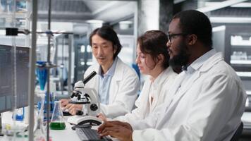 Senior researcher records observations from coworkers using microscope to evaluate cellular structures. Man taking notes of medical tissue observation through magnification tool, camera B video