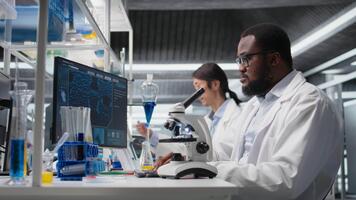 klinisk mikrobiolog i labb använder sig av mikroskop för patologi forskning, ser på molekyl data. forskning anläggning professionell använder sig av optisk enhet redskap till undersöka testa exemplar, kamera en video