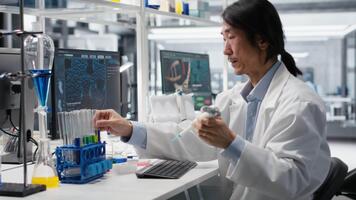 labb ingenjör gör pipettering procedur med kemisk reagens, blandning lösningar för reaktion testning. senior forskare användningar pipett till överföra flytande in i testa rör, skakning till blandning, kamera b video