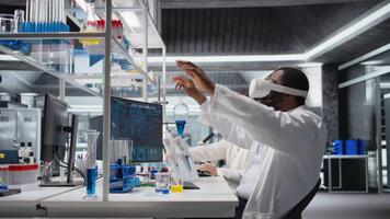 Wissenschaftler mit Computer und vr Headset Ausrüstung zum DNA Daten Analyse im Labor. afrikanisch amerikanisch Mann mit Bioinformatik Genomik Software und virtuell Wirklichkeit Technik im modern Labor, Kamera ein video