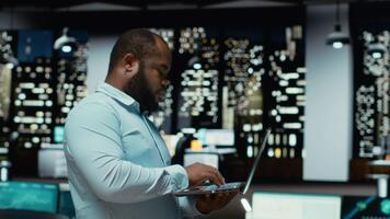 schwarz Kerl Prüfung archiviert Unterlagen Vor transkribieren auf pc Notizbuch, Notizen und extrahieren das Main Punkte von Berichte auf Laptop. Analytiker dokumentieren nach Std spät beim Nacht. Kamera b. video